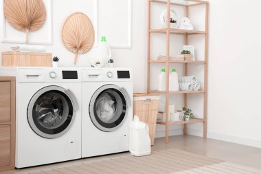 Çamaşır makinesi, ahşap dolap ve raf ünitesi olan bir çamaşırhane.