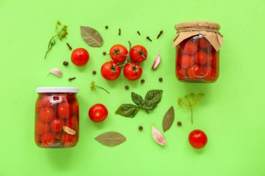 Yeşil arka planda konserve domates, fesleğen ve sarımsak olan kavanozlar.