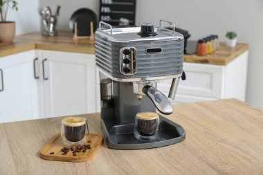 Mutfaktaki masada bir bardak sıcak espresso ile modern kahve makinesi.