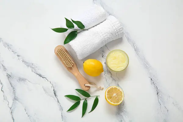 Bowl of lemon body scrub, massage brush and towels on grunge white background