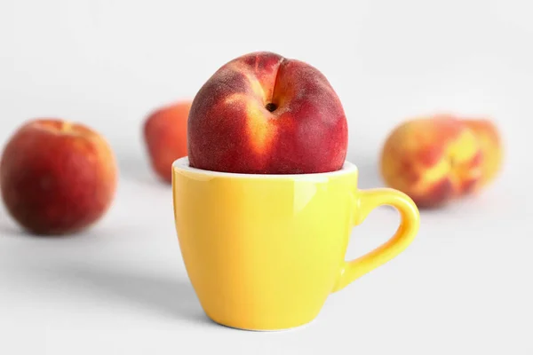 Cup with sweet peaches on white background