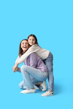 Küçük kız ve annesi mavi arka planda örülü süveter giyip sarılıyorlar.