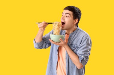 Young man eating Chinese noodles on yellow background