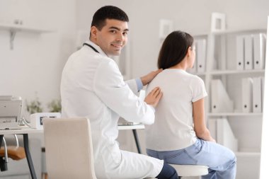 Erkek doktor klinikteki genç kadının duruşunu kontrol ediyor.