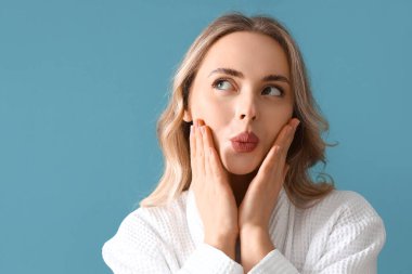 Mavi arka planda yüz geliştirme egzersizi yapan genç kadın, yakın plan.