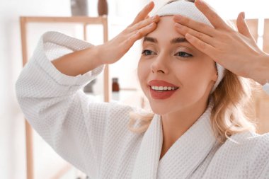 Banyoda yüz geliştirme egzersizi yapan genç bir kadın.