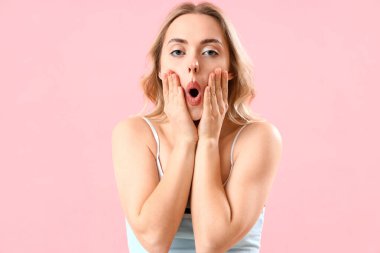 Pembe arka planda yüz geliştirme egzersizi yapan genç bir kadın.