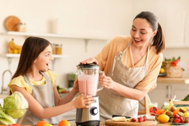 Küçük kız ve annesi mutfakta blender ile smoothie yapıyorlar.