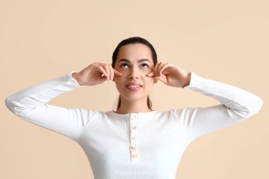 Bej arka plan üzerinde yüz geliştirme egzersizi yapan genç bir kadın.