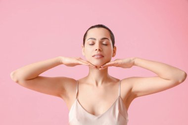 Pembe arka planda yüz geliştirme egzersizi yapan genç bir kadın.