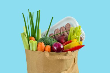 Mavi arka planda içi taze sebze ve sosis dolu kağıt torba.