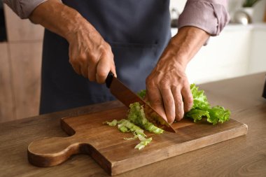 Olgun adam mutfakta marul kesiyor, yakın plan.