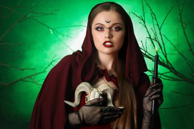 Yeşil arka planda mum ve koyun kafatası ile güzel genç cadı