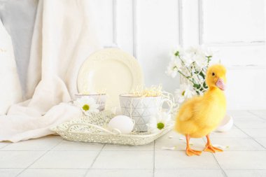 Şirin ördek yavrusu, bardaklı tepsi ve beyaz fayans üzerinde papatya çiçeği.