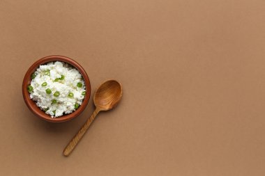 Kahverengi arka planda bir kase lezzetli süzme peynir.