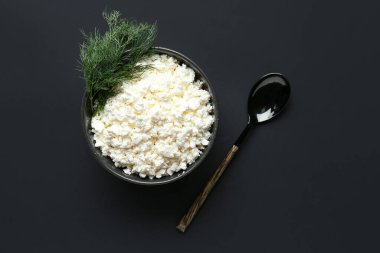 Siyah arka planda bir kase lezzetli süzme peynir.