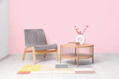 Grey armchair, coffee table and stylish rug near pink wall