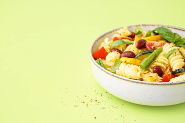 Bir kase domatesli makarna salatası ve yeşil arka planda fesleğen.