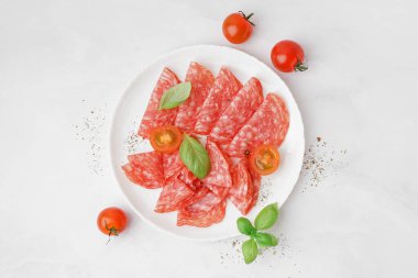 Plate with slices of tasty salami on light background