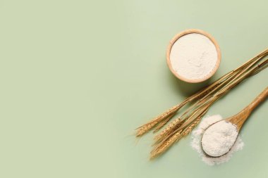 Bowl and spoon with wheat flour on green background