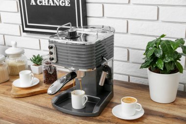 Modern coffee machine with cups of hot espresso on table in kitchen