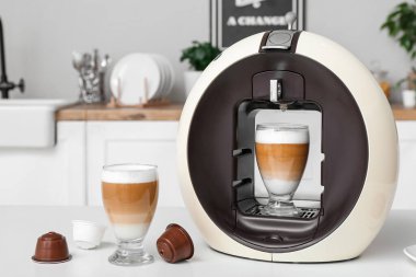 Modern coffee machine with glasses of hot latte on table in kitchen