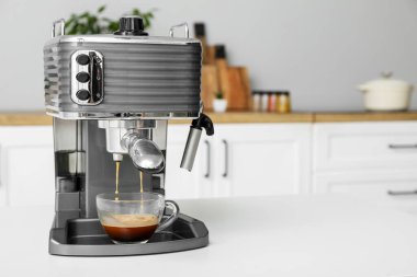 Modern coffee machine with glass cup of hot espresso on table in kitchen
