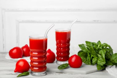Glasses of tasty tomato juice on white wooden background
