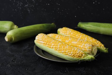 Plate with fresh corn cobs on black background