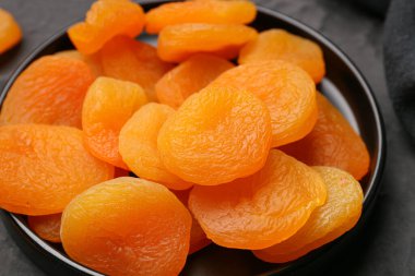 Tray with tasty dried apricots on black background