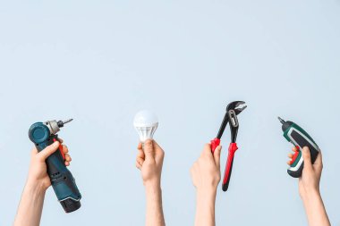 Electrician hands with light bulb and tools on grey background