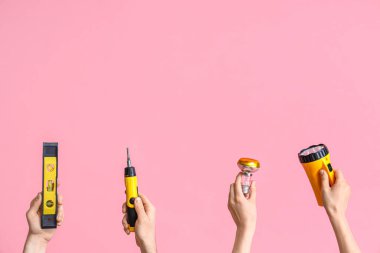 Electrician hands with tools on pink background