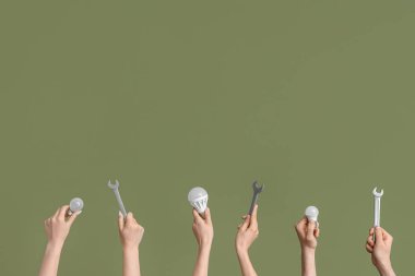 Electrician hands with light bulbs and wrenches on green background