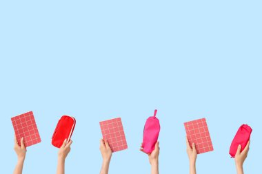 Hands with pencil cases and notebooks on blue background