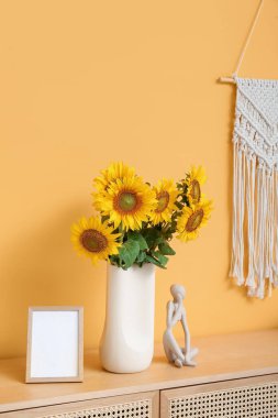 Vase with sunflowers, frame and decor on chest of drawers in living room