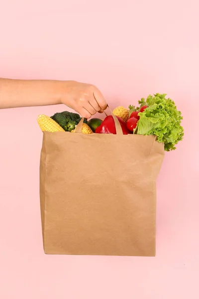 ピンクの背景に新鮮な野菜でいっぱいの紙袋が付いている女性の手 — ストック写真