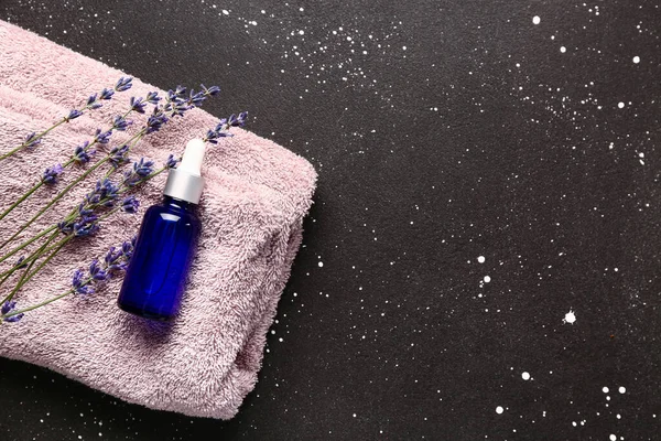 Bottle of essential oil, clean towel and lavender flowers on dark background