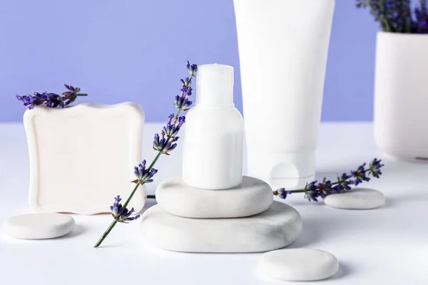 Composition with cosmetic products, spa stones and lavender flowers on light table against color background