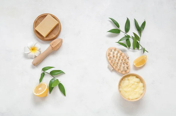 Bowl of lemon body scrub with massage brush, juicer and soap on white background