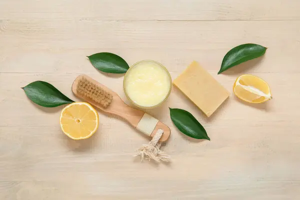 Bowl of lemon body scrub with massage brush and soap on beige wooden background