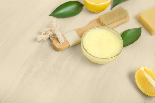 Bowl of lemon body scrub with massage brush and soap on beige wooden background