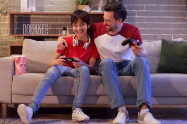 Küçük çocuk ve babası akşam evde video oyunu oynuyorlar.