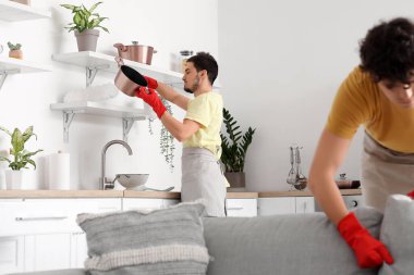 Erkek hademe, mutfakta pp-toz bezi ile rafı temizliyor.