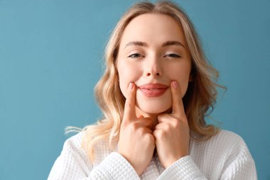 Mavi arka planda yüz geliştirme egzersizi yapan genç kadın, yakın plan.