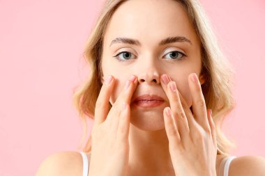 Pembe arka planda yüz geliştirme egzersizi yapan genç kadın, yakın plan.