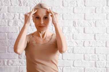 Olgun kadın beyaz tuğla arka planda yüz geliştirme egzersizi yapıyor.