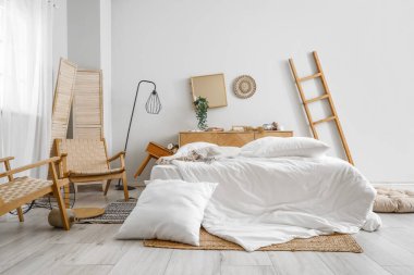 Yatak, koltuk ve yastıklı dağınık bir yatak odası.