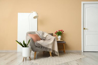 Gri koltuk ve vazo, bej duvarın yanındaki gri koltukta lale çiçekleri.