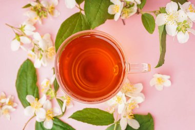 Bir bardak çay ve pembe arka planda güzel yasemin çiçekleri.