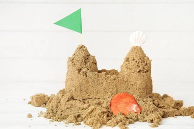 Kumdan yapılmış deniz kabukları ve beyaz ahşap arka planda bayrak.